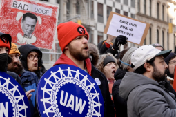 A group of 20 protesters with UAW and Save Our Services signs, many are yelling