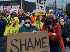 Workers gather in a March 27 protest holding signs reading "Shame" and "Melt ICE!"