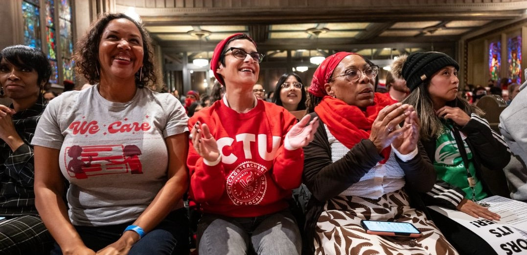 Five women sit applauding, one is wearing a CTU T-shirt, another says “we care” with a drawing of a chalkboard