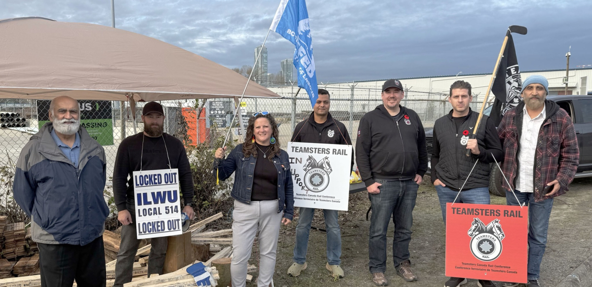 A group of people hold picket signs in front of a canopy. A group of people hold picket signs in front of a canopy.
