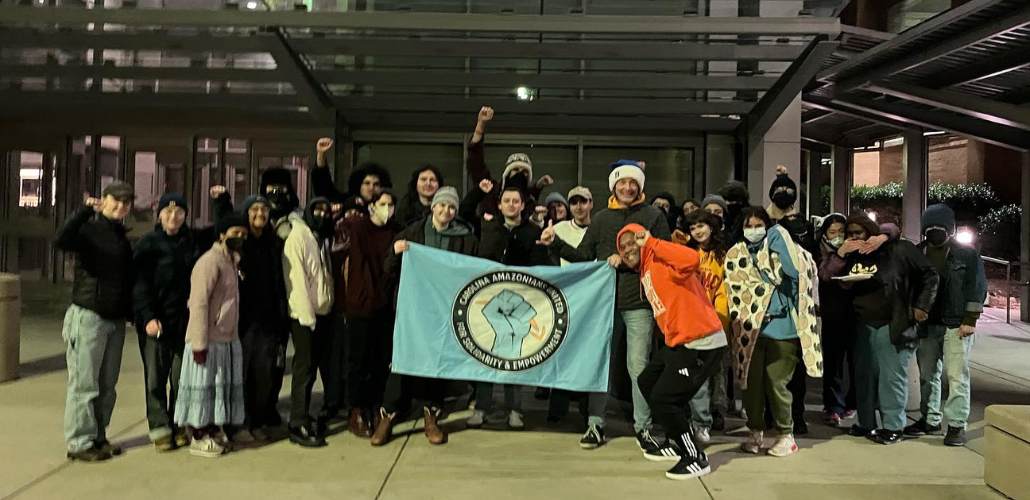 Trabajadores de Amazon y simpatizantes de la comunidad se reúnen sosteniendo una pancarta con la leyenda CAUSA de Amazon.
