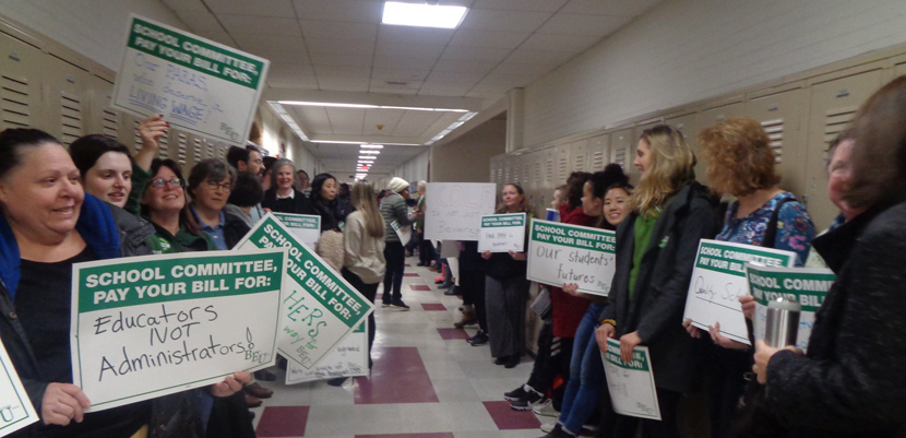 Brookline paraeducators with signs lining hallway of school.