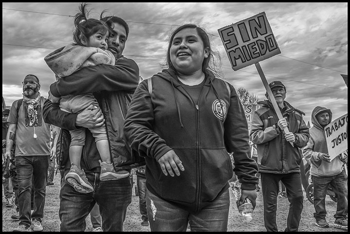 Lelo Juarez stands with his wife and child at a May Day march. Behind him, someone holds a sign reading "without fear" in Spanish.