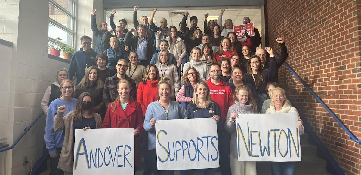 Two dozen teachers stand on stairs with signs saying ‘Andover Supports Newton’