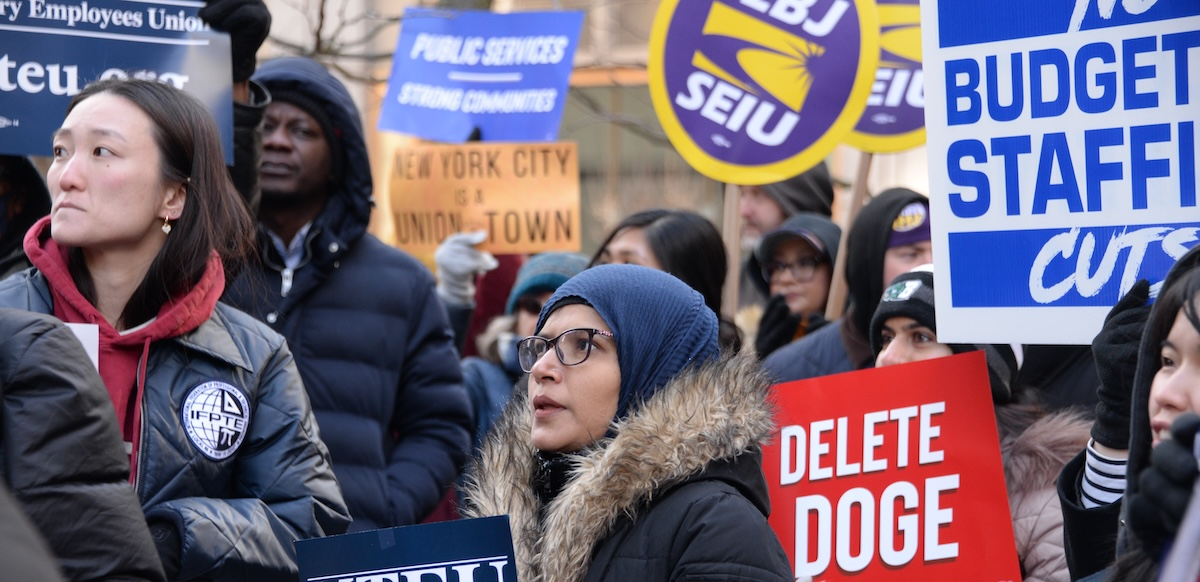 A group of worried-looking protesters hold signs about government cuts