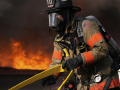 A firefighter in full protective equipment moves a yellow hose with fire in the background